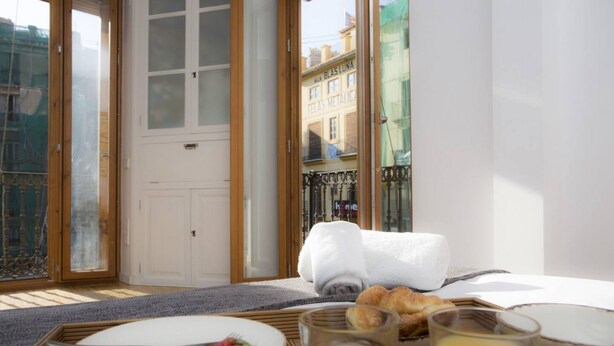 A breakfast setup with croissants, strawberries, and orange juice on a wooden table, with a view of a city street and a white door in the background. - Singular Stays El Balcon de Manet (Valencia / València)