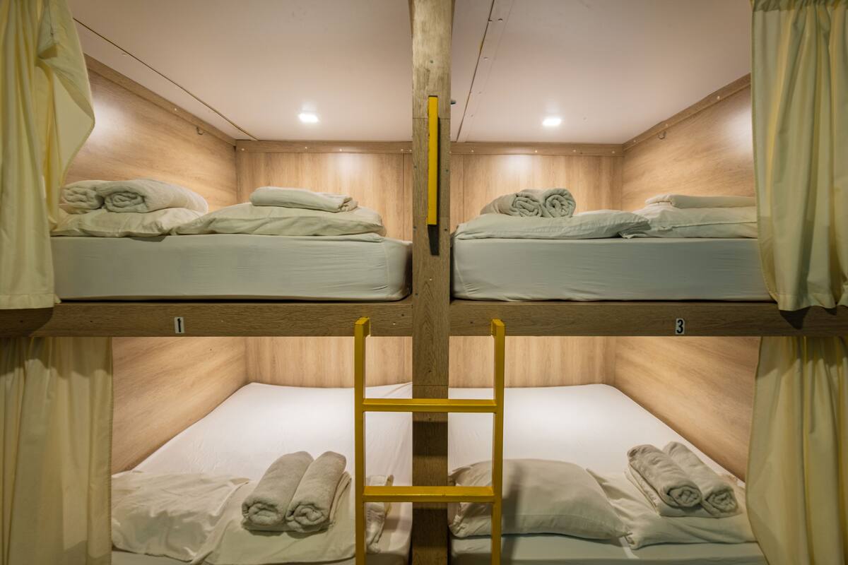 A bunk bed room with wooden walls, a central ladder, and neatly made beds with towels.