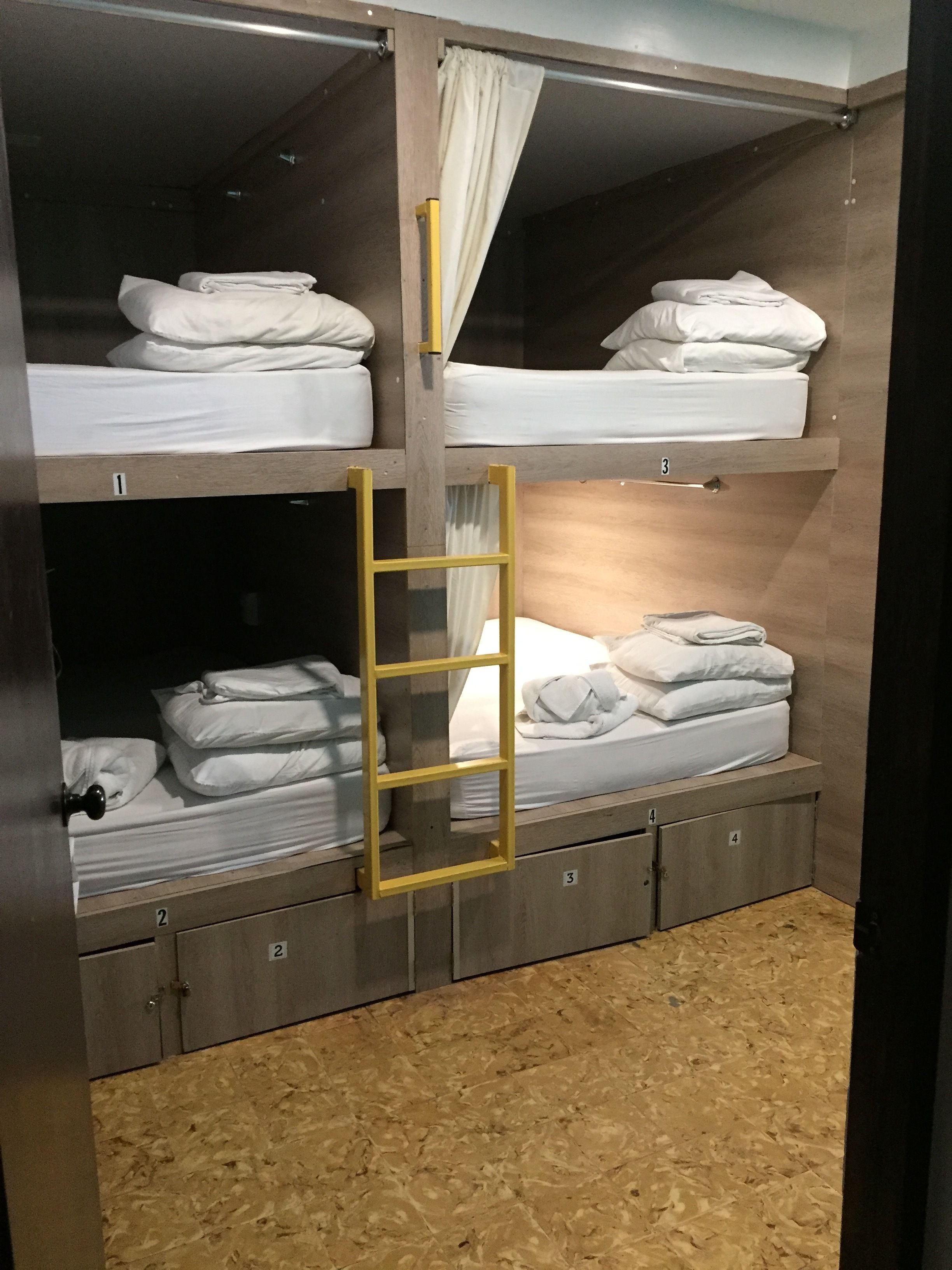 Habitación con literas, un escalón, compartimentos de almacenamiento numerados y una cortina.