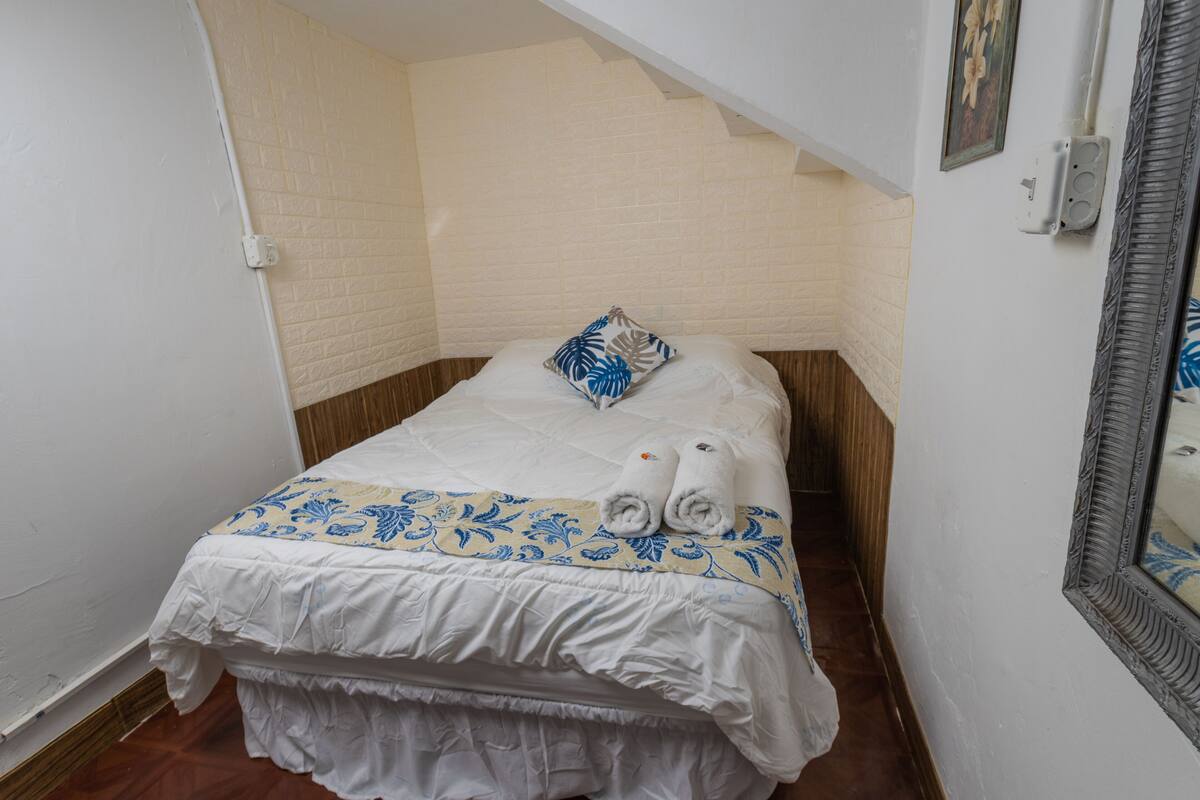 A small, neatly made bed with a white and blue patterned bedspread, a pillow, and two rolled towels.