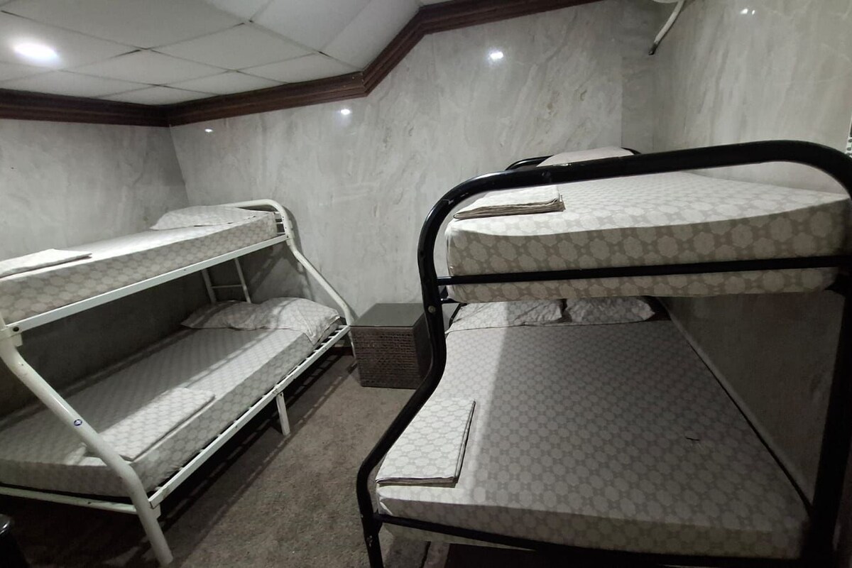 A bunk bed room with a mattress on the top bunk and a desk with a chair.