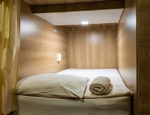A small, wooden-paneled room with a single bed, a white pillow, and a rolled towel. - Hostel the pod 33 (Panama City)