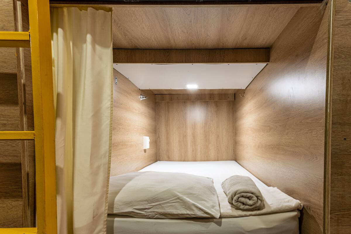 A compact, wooden-paneled room with a single bed, a small window, and a curtain.