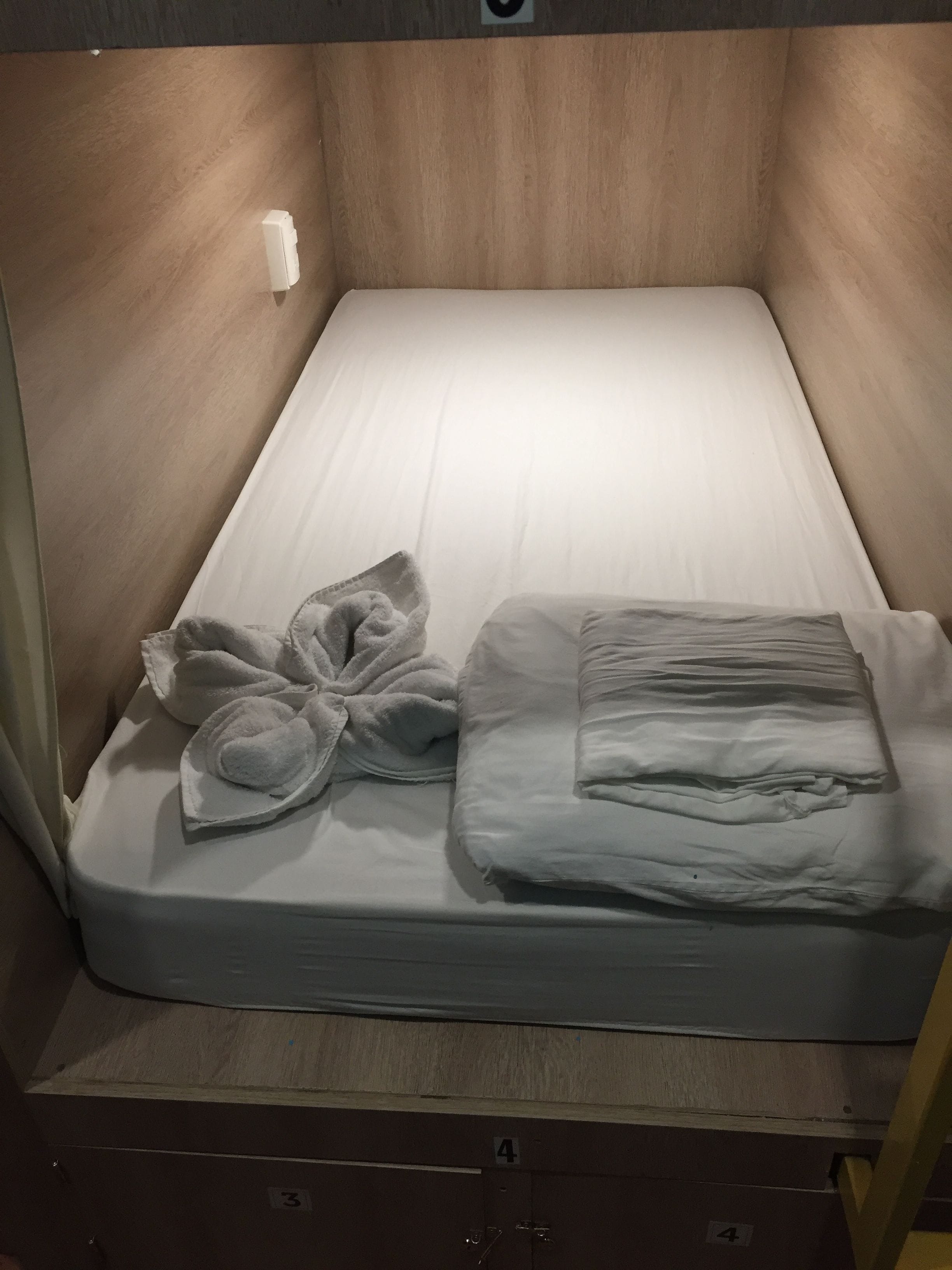A single bed with a white mattress and pillows, a wooden headboard, and a small white object on the wall.