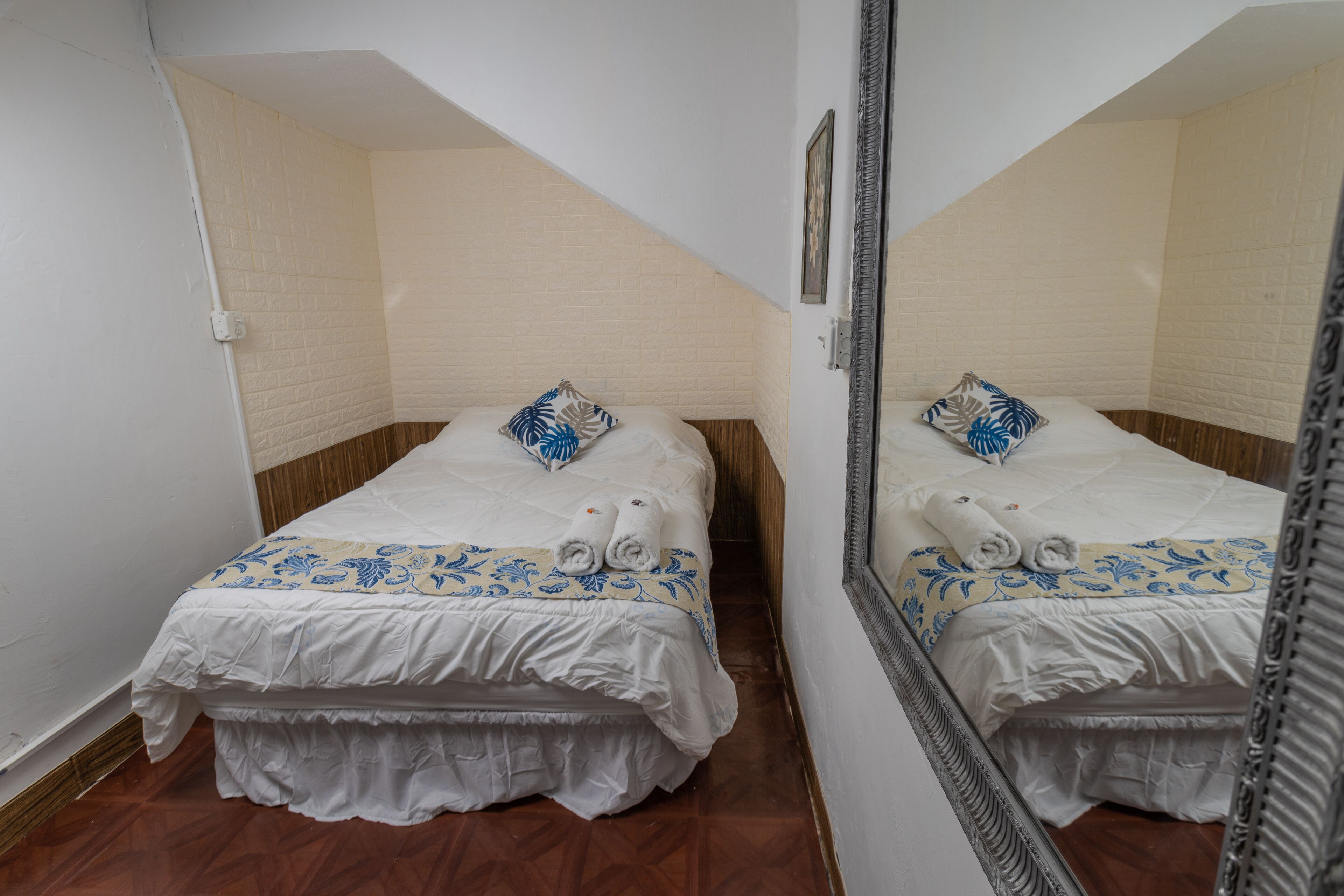 A bedroom with a mirrored wall, a bed with a patterned bedspread, and a wooden headboard.