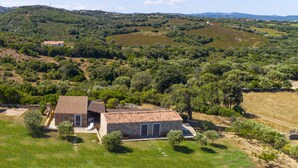 A stone house with a tiled roof, surrounded by lush greenery and hills in the background. - "Mirto" house in the Stazzu Gallurese style in the countryside only 3.5 km from the sea (Rena Majore Aglientu)