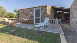 A stone building with a patio area, including two white lounge chairs, a table, and a small seating area with a chair and a table. - "Mirto" house in the Stazzu Gallurese style in the countryside only 3.5 km from the sea (Rena Majore Aglientu)