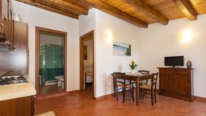 A kitchen with wooden cabinets, a dining area with a table and chairs, and a TV on a wooden cabinet. - "Mirto" house in the Stazzu Gallurese style in the countryside only 3.5 km from the sea (Rena Majore Aglientu)