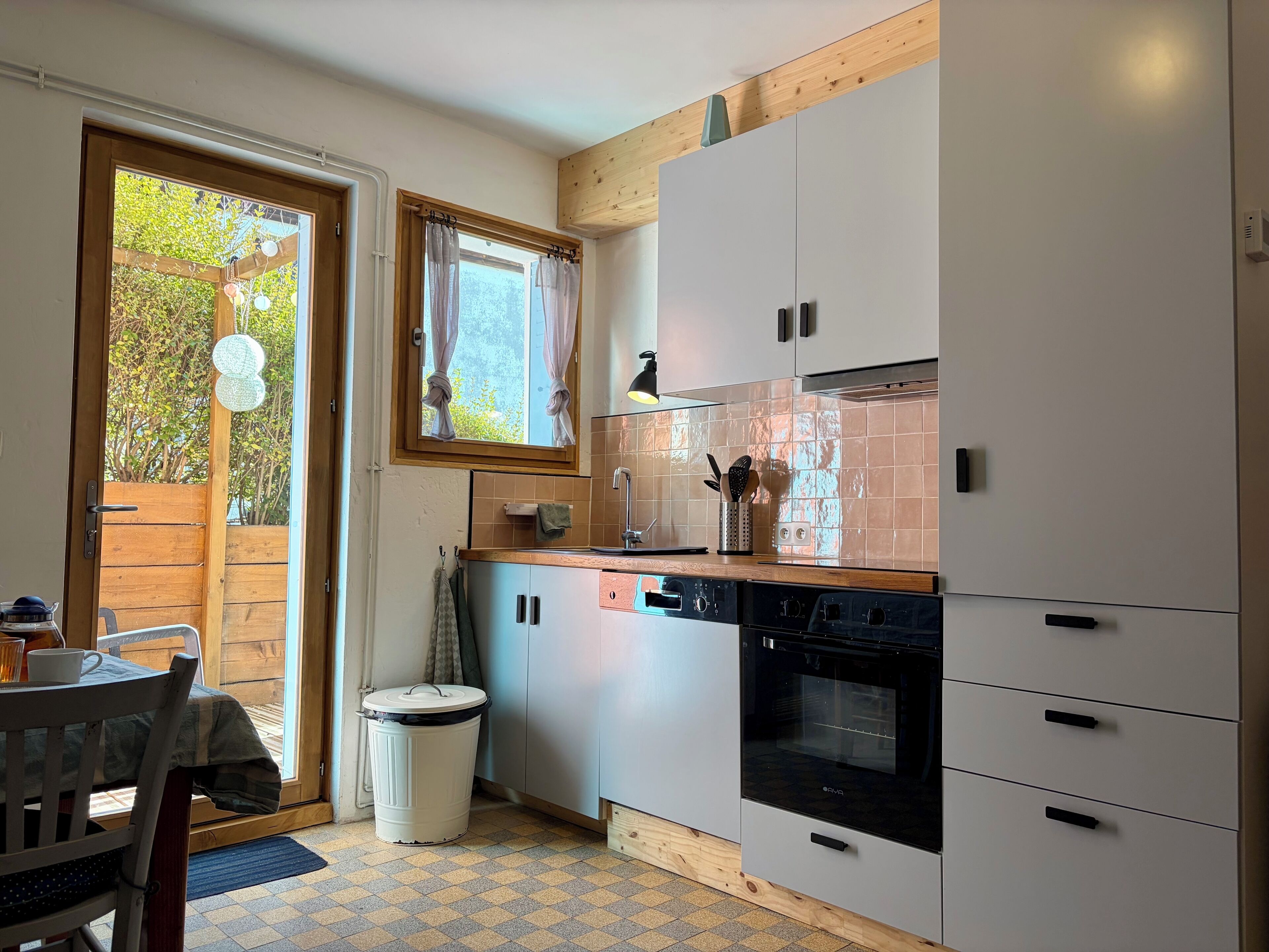 A compact kitchen with white cabinets, a wooden countertop, a built-in oven, and a window with curtains.