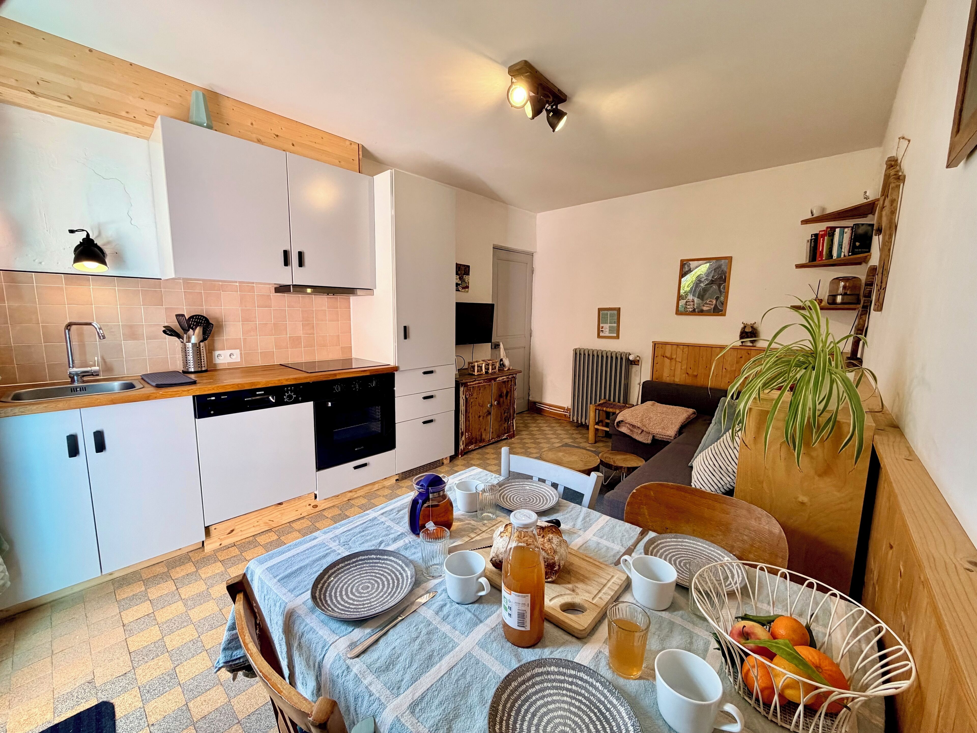 A compact kitchen with white cabinets, a wooden countertop, and a dining area with a table set for two.