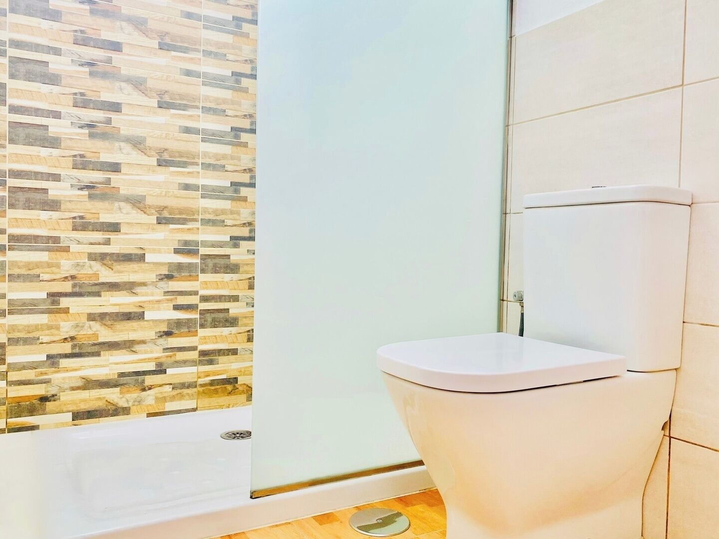 Een badkamer met betegelde douchewand, toilet en douchedeur.