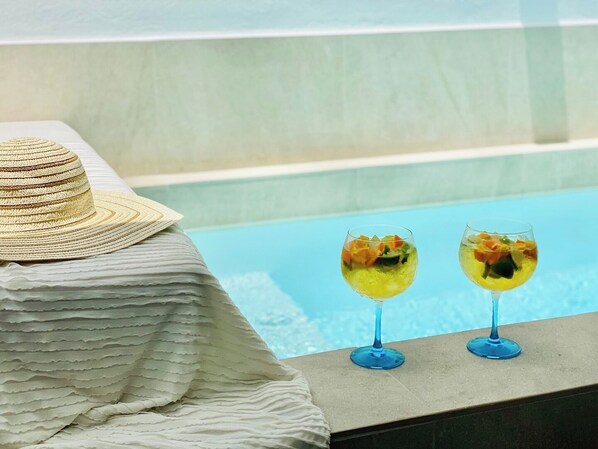 Escena junto a la piscina con un sombrero de paja y dos vasos de una bebida amarilla sobre un borde de piedra.