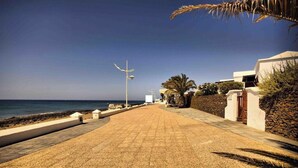 Ein gepflasterter Weg entlang der Küste mit freiem Blick auf das Meer, einer Straßenlaterne und einem Gebäude mit Steinmauer und Holztor.