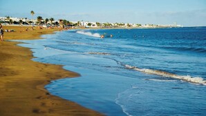 Ein Strand mit Wellen, Personen und Gebäuden im Hintergrund.