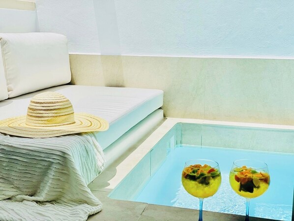 A poolside area with a white sofa, a straw hat, and two drinks on a table.