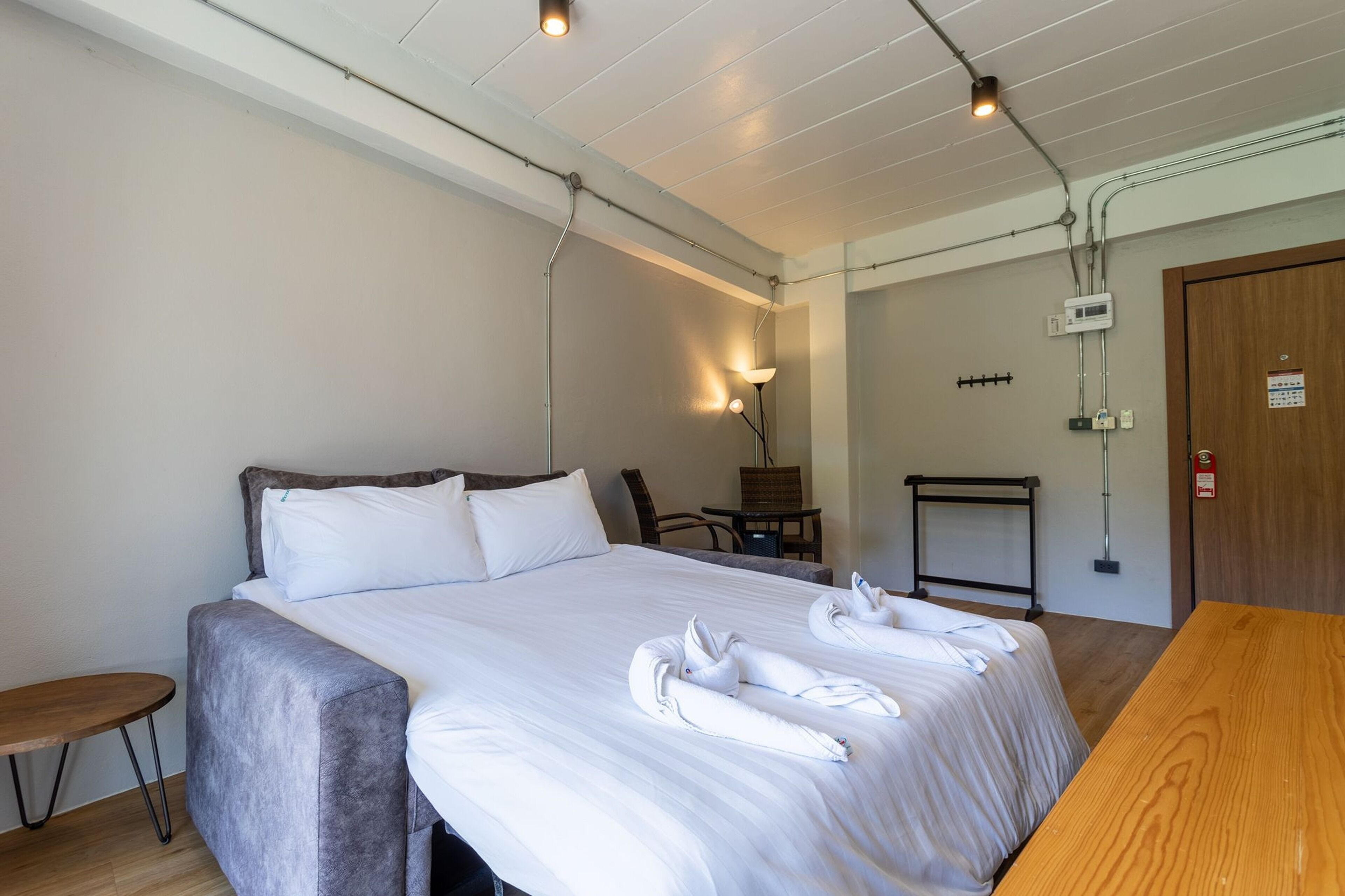 Una cama bien hecha con sábanas blancas y dos toallas dispuestas sobre ella. Hay un banco de madera y una mesita de noche junto a la cama.