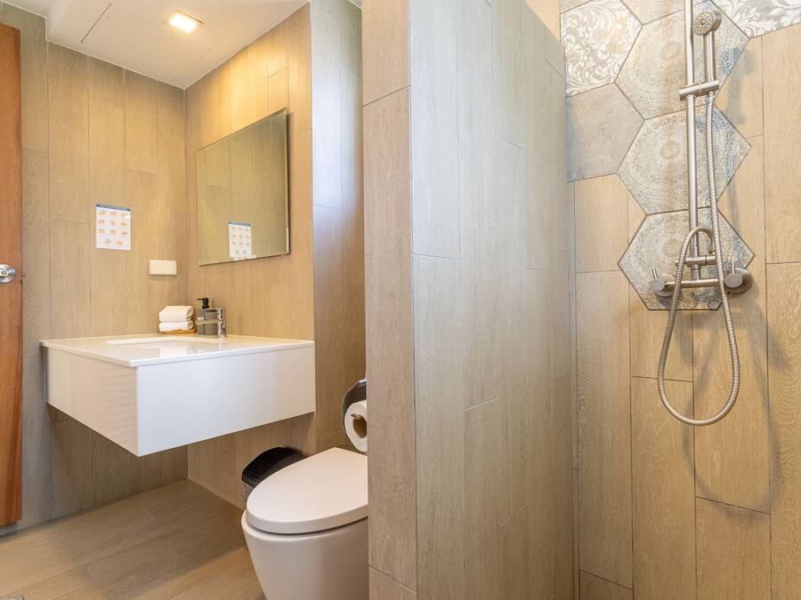 A modern bathroom with a wooden door, a white sink with a mirror, a toilet, and a shower with a hexagonal tile pattern.