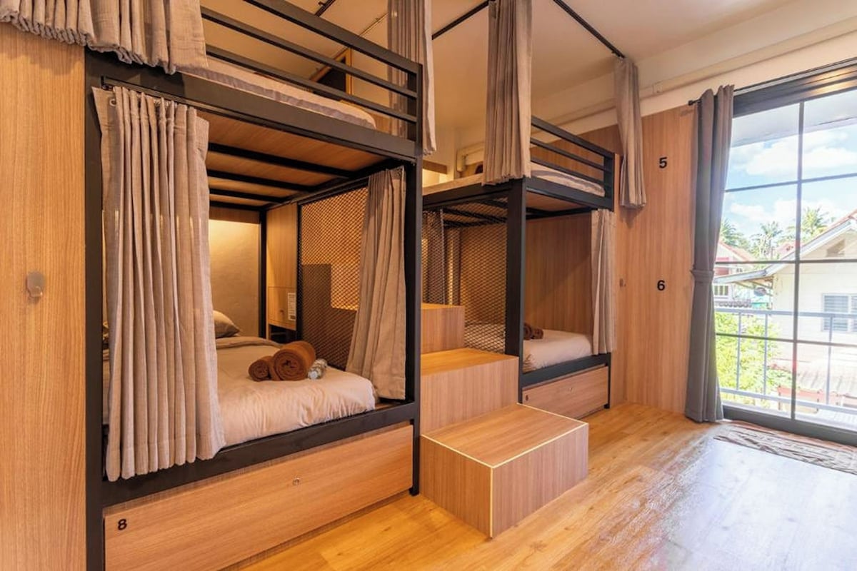 A room with bunk beds, a wooden floor, and a window with a view of buildings.