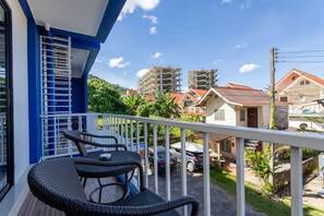 Un balcón con mobiliario de mimbre, vista a una zona residencial y un edificio en construcción al fondo.