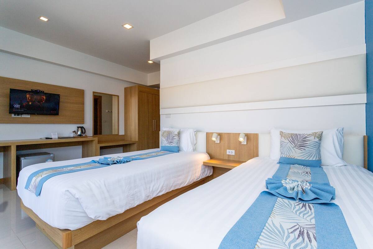 Ein modernes Hotelzimmer mit zwei Einzelbetten, einem an der Wand befestigten Fernseher und einem Holztisch mit Wasserkocher.