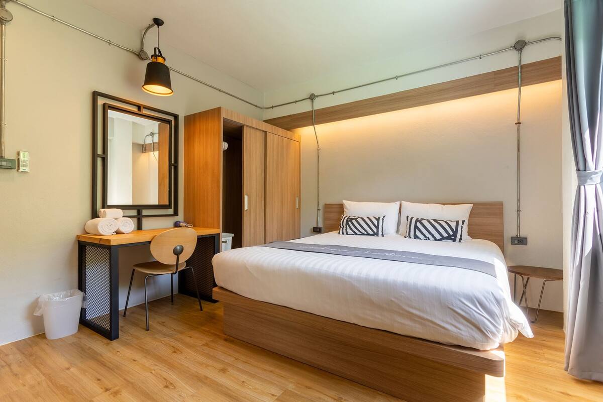 Ein modernes Schlafzimmer mit einem hölzernen Bett, einem Schreibtisch mit Stuhl, einem Spiegel und einer Pendelleuchte.