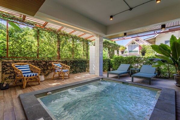 Zona de piscina al aire libre con sillones de descanso y un pérgola cubierta de follaje.