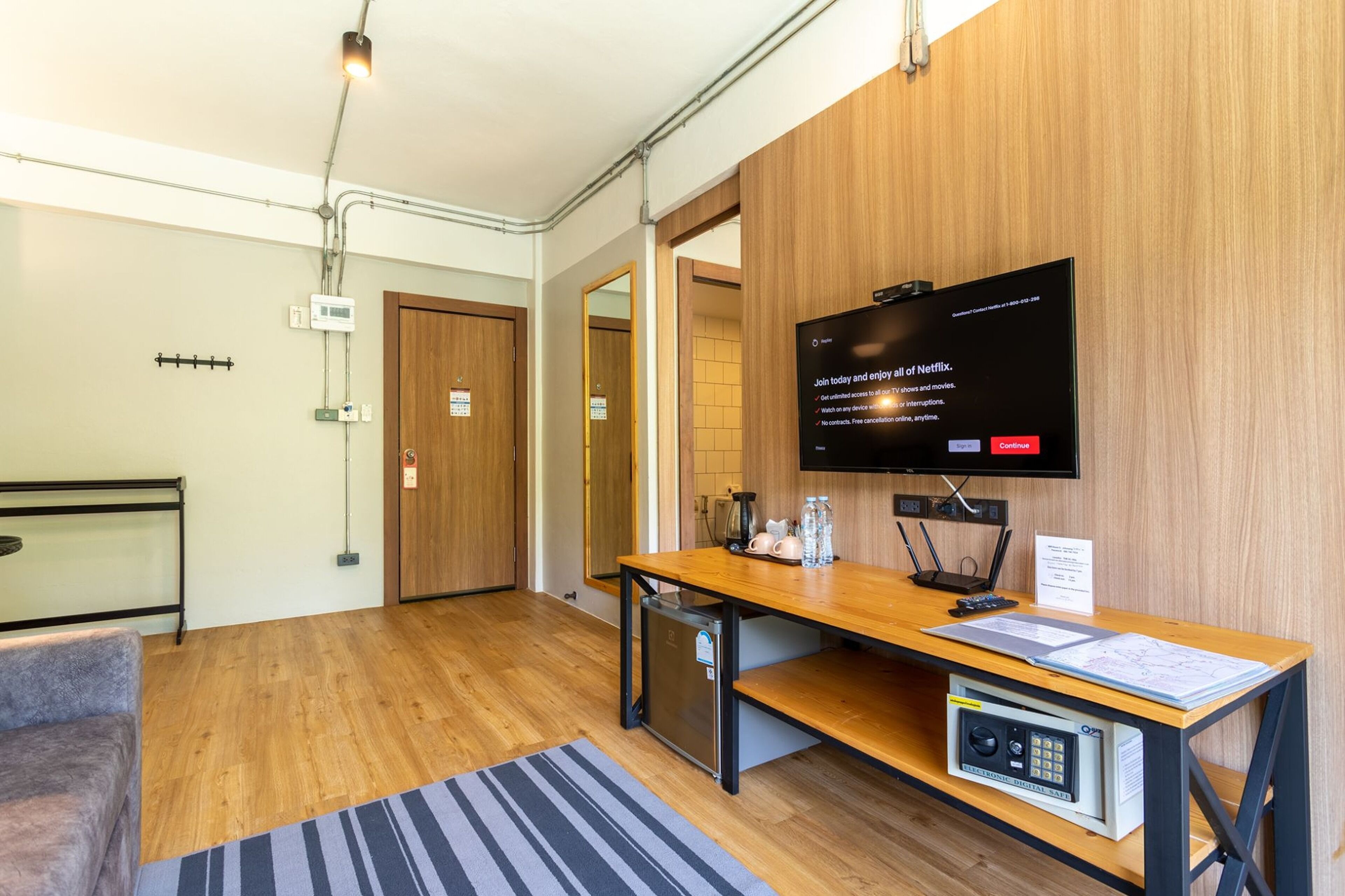 A modern hotel lobby with a wooden reception desk, a television displaying a Netflix advertisement, and a small refrigerator.