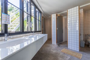 A modern bathroom with a large white sink, a window with a view of greenery, and a tiled shower area.