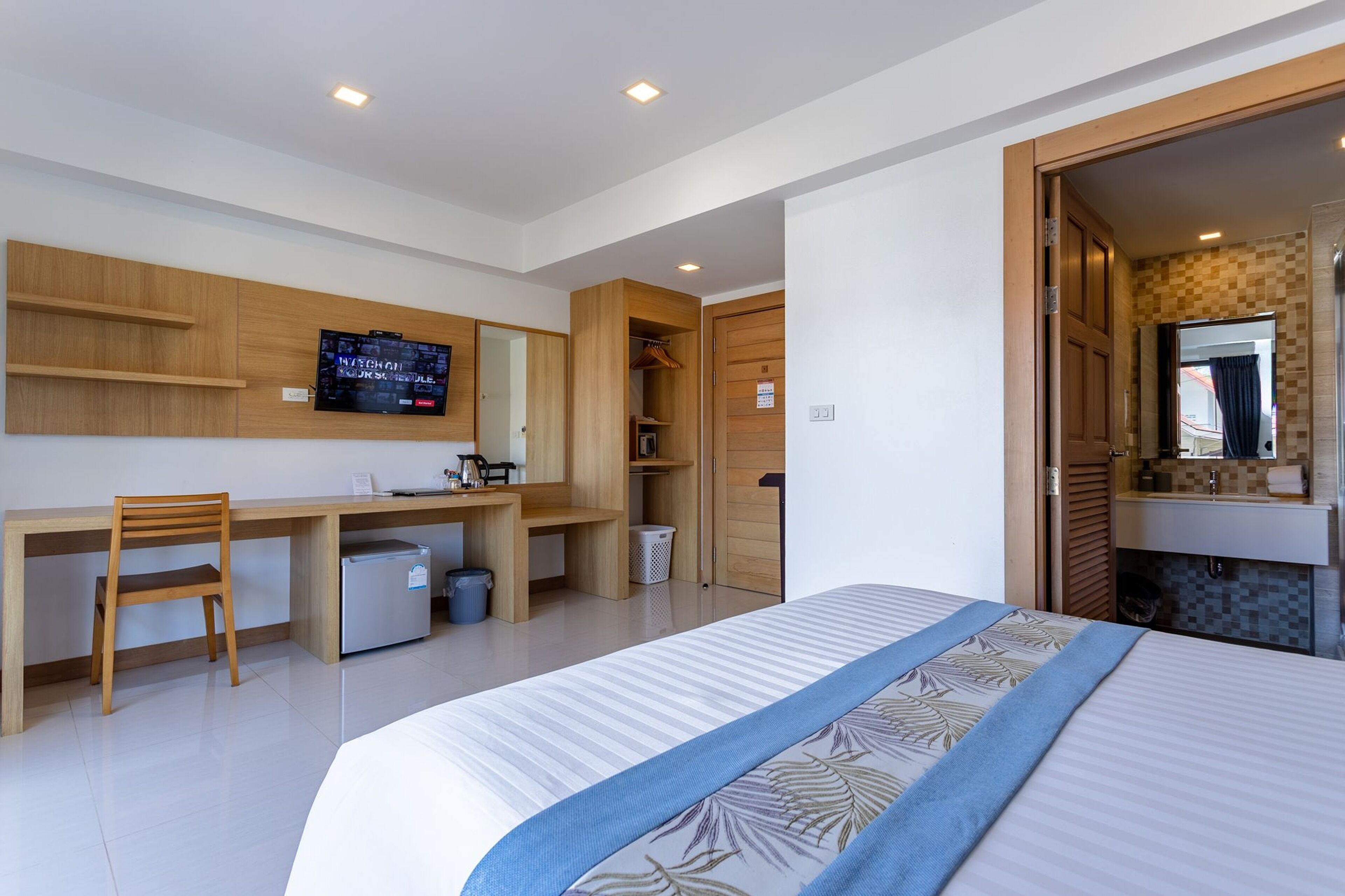 A modern hotel room with a bed, a desk with a chair, a television, and a wardrobe.
