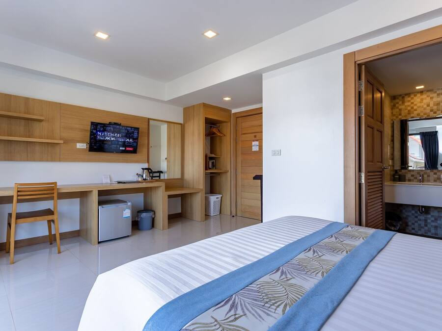 A modern hotel room with a bed, a desk with a chair, a television, and a wardrobe.