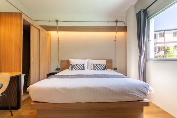A modern bedroom with a wooden bed, white bedding, and a view of a building outside. - Aonang Guesthouse (Krabi)
