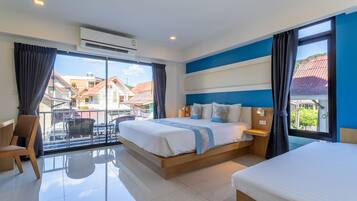 Habitación de hotel con una cama grande, otra más pequeña, una silla, una mesa y un balcón con vistas a edificios.