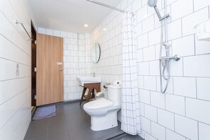Un baño moderno con azulejos blancos, una puerta de madera, un inodoro, un lavabo y una ducha.