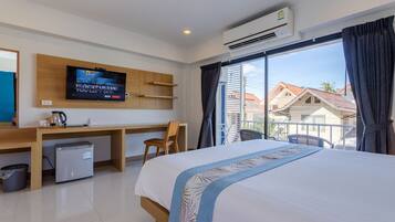 Habitación de hotel con cama, escritorio con televisor, refrigerador pequeño y vista a casas por la ventana.