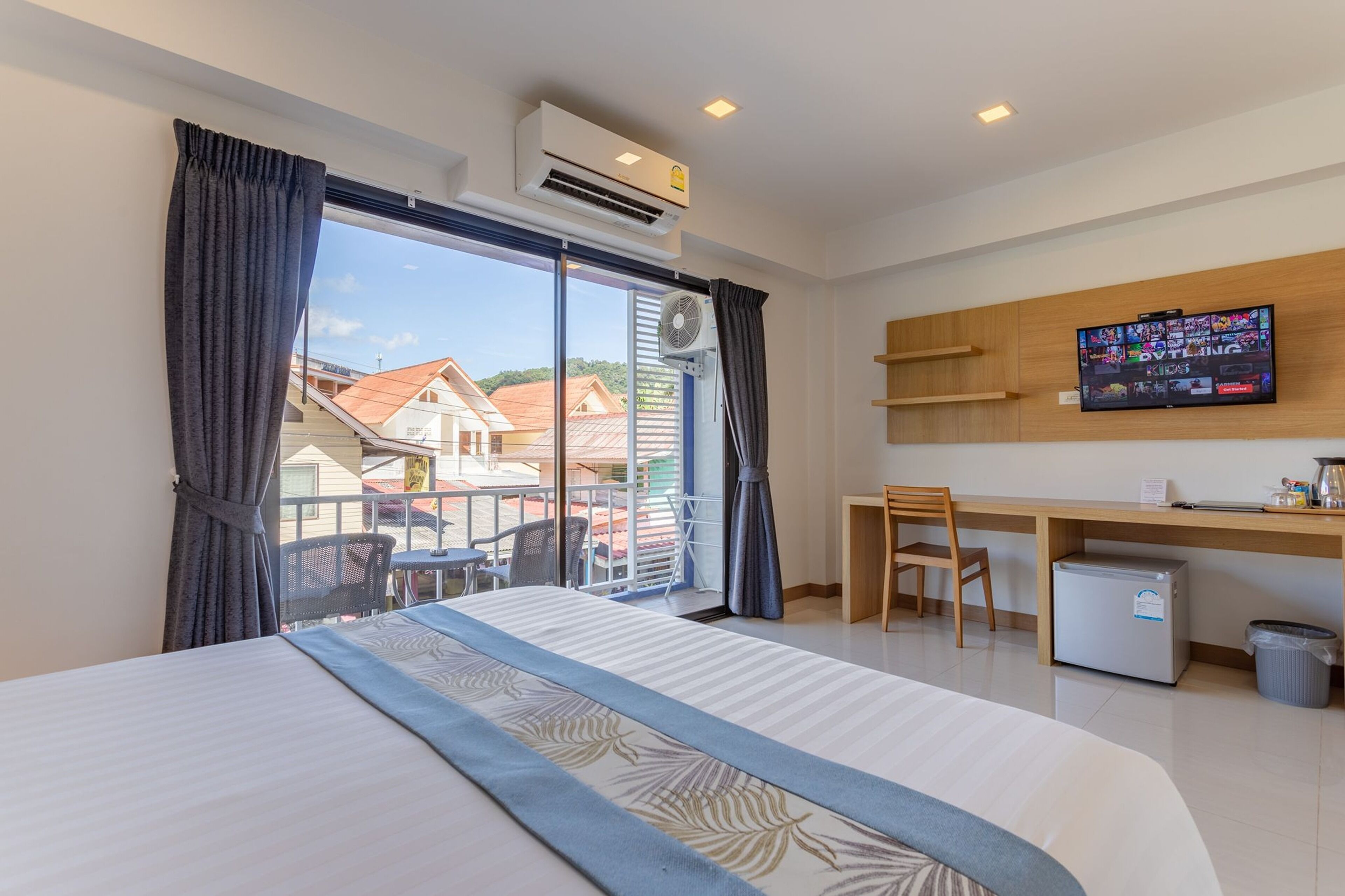 Ein Hotelzimmer mit Bett, Schreibtisch, Stuhl, Fernseher und einem Balkon mit Blick auf Häuser.
