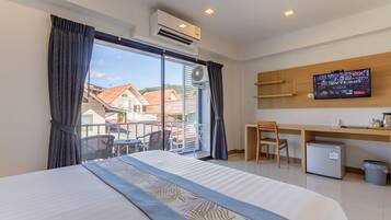 Ein Hotelzimmer mit Bett, Schreibtisch, Stuhl, Fernseher und einem Balkon mit Blick auf Häuser.