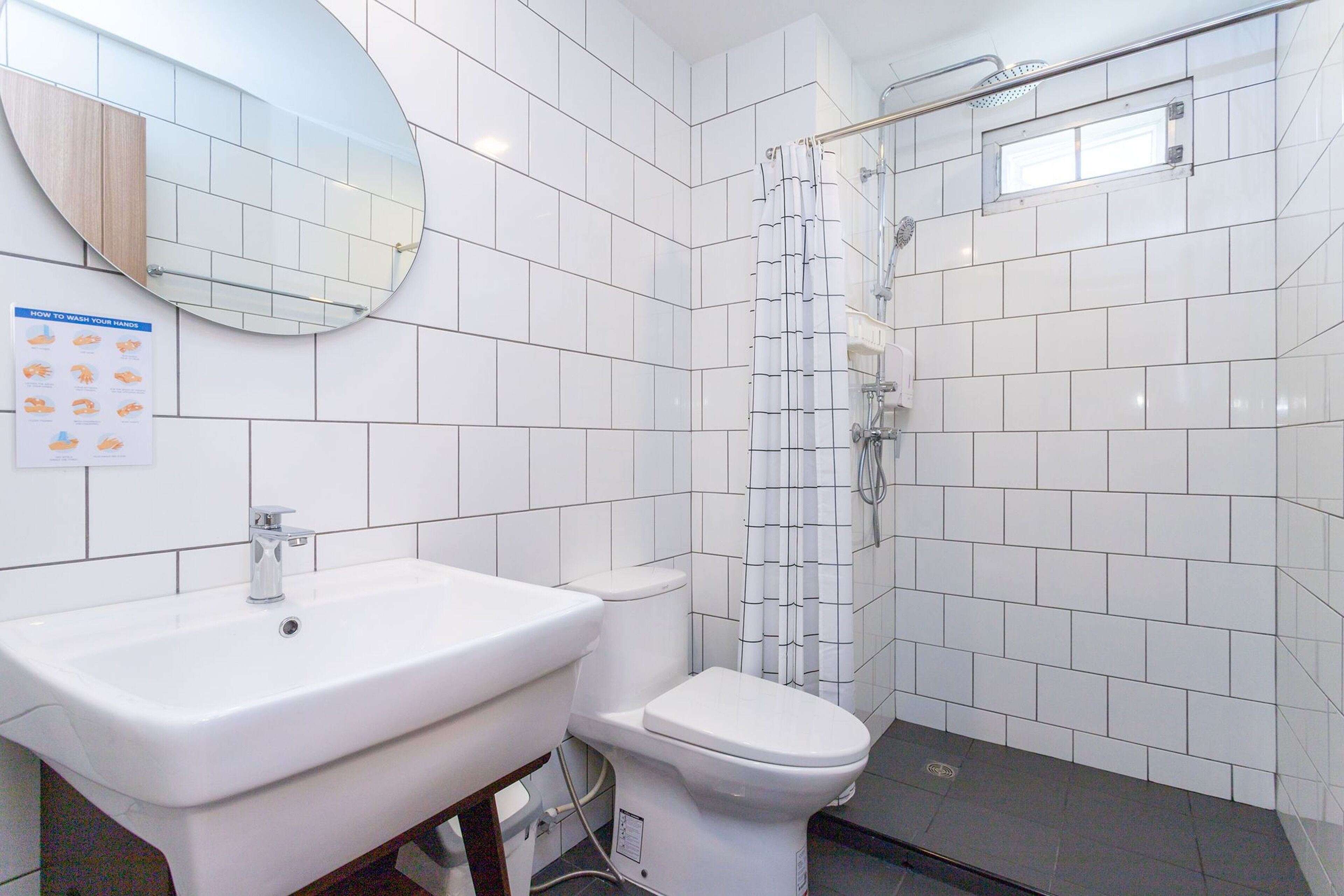 A bathroom with a white sink, toilet, and shower. There is a mirror above the sink and a poster on the wall.