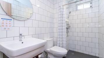 A bathroom with a white sink, toilet, and shower. There is a mirror above the sink and a poster on the wall.