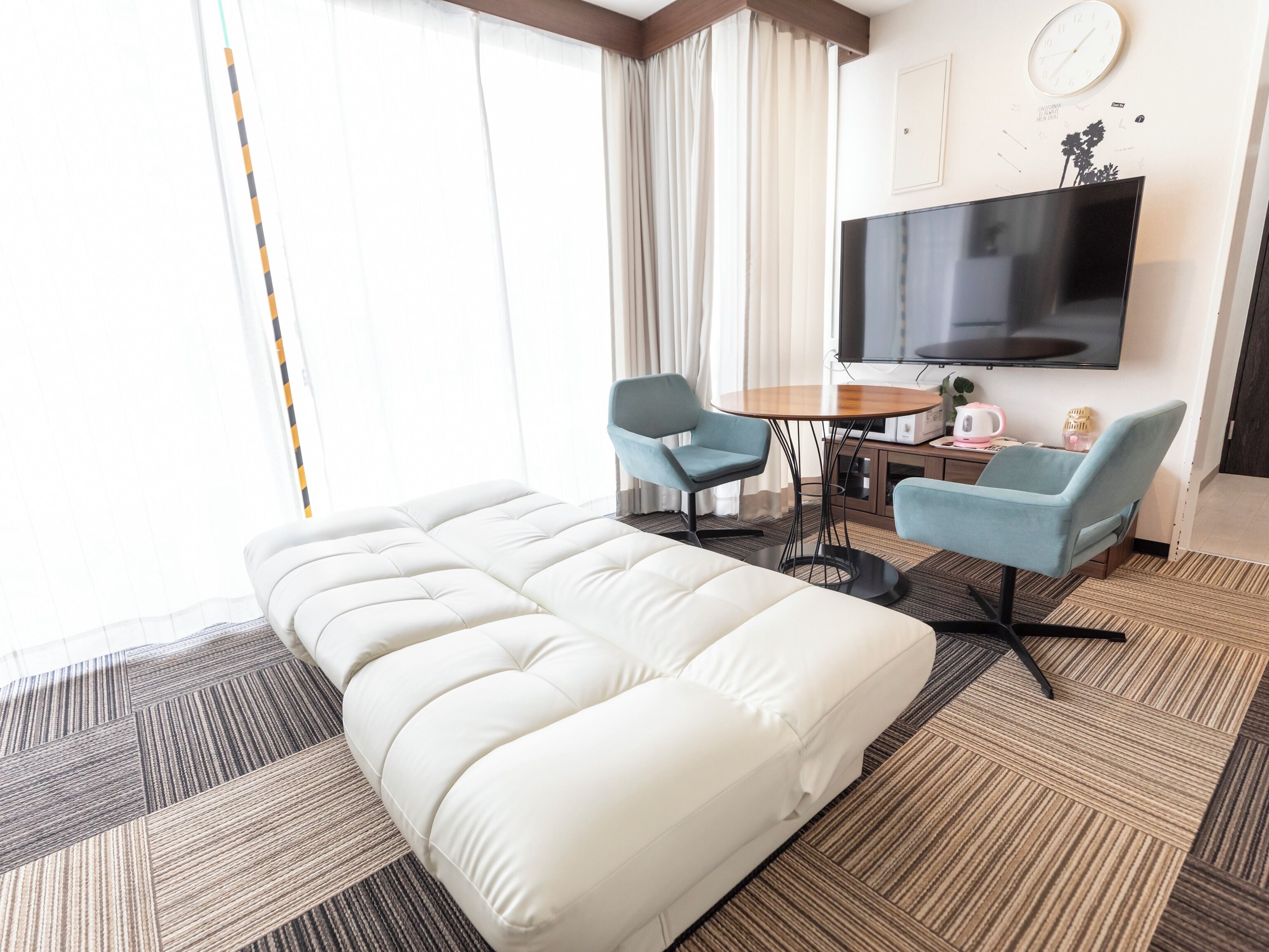 A hotel room with a large bed, two armchairs, a small table, a TV, and a clock on the wall.