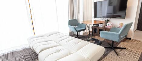 A hotel room with a large bed, two armchairs, a small table, a TV, and a clock on the wall.