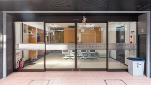 A hotel entrance with a reception desk, a fire extinguisher, and a trash bin. - Tabist Sakuragawa River Side Hotel (Osaka)