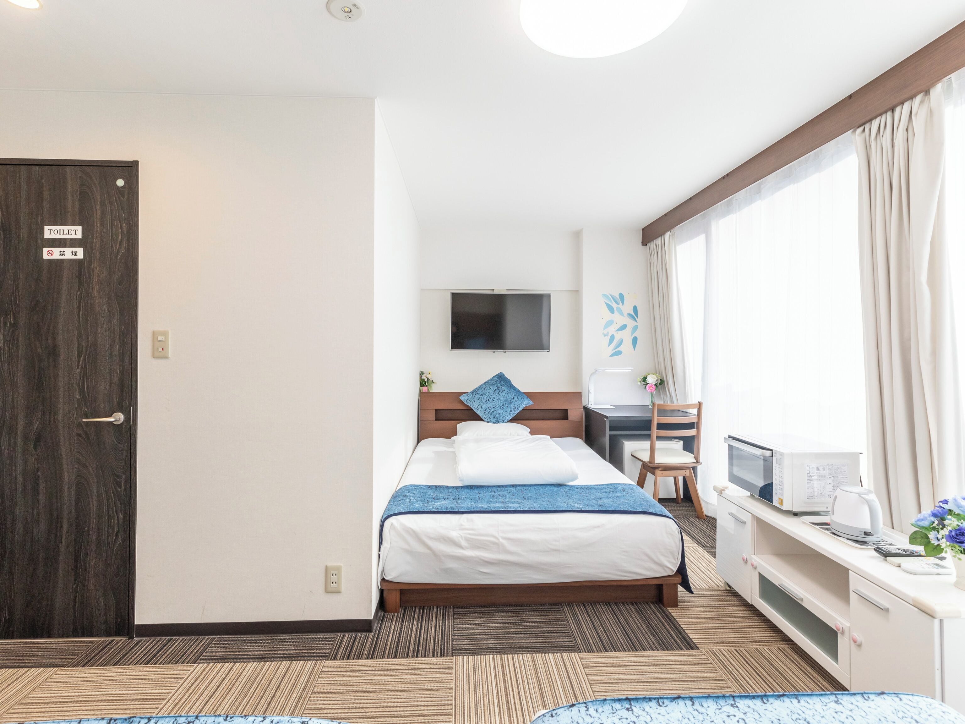 Ein Hotelzimmer mit Bett, Schreibtisch, Fernseher und einem Fenster mit Vorhängen.
