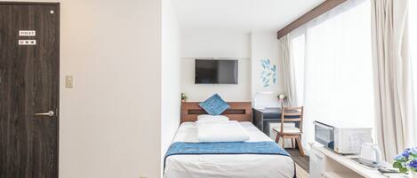 Ein Hotelzimmer mit Bett, Schreibtisch, Fernseher und einem Fenster mit Vorhängen.