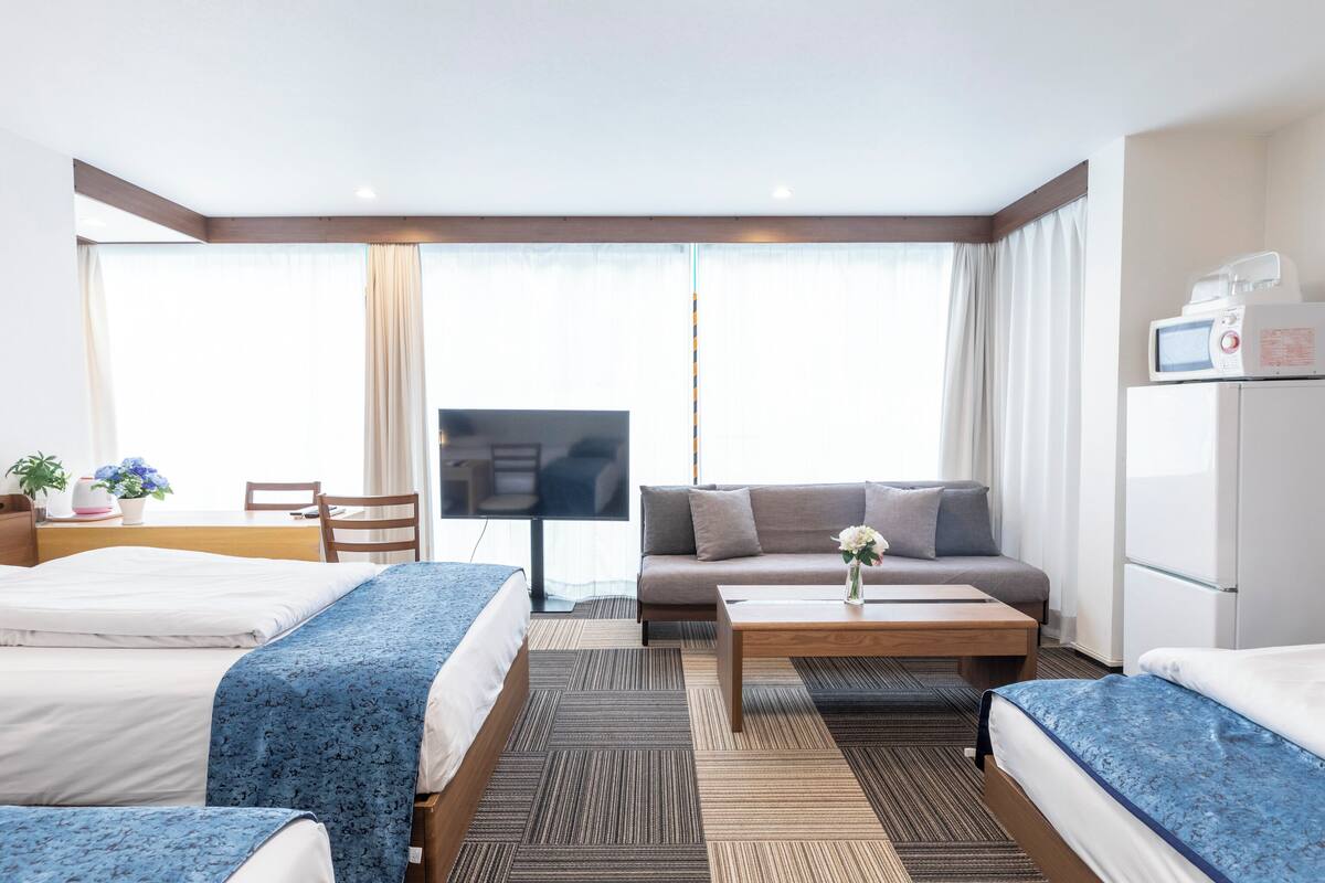 A hotel room with two beds, a sofa, a coffee table, a TV, and a refrigerator.