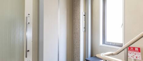 A hotel room with a sliding door, a small black trash bin, a window with a view, and a fire extinguisher on the wall.
