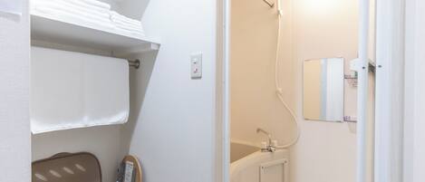A bathroom with a shower, a sink, and a toilet. There is a towel rack and a shelf with folded towels.