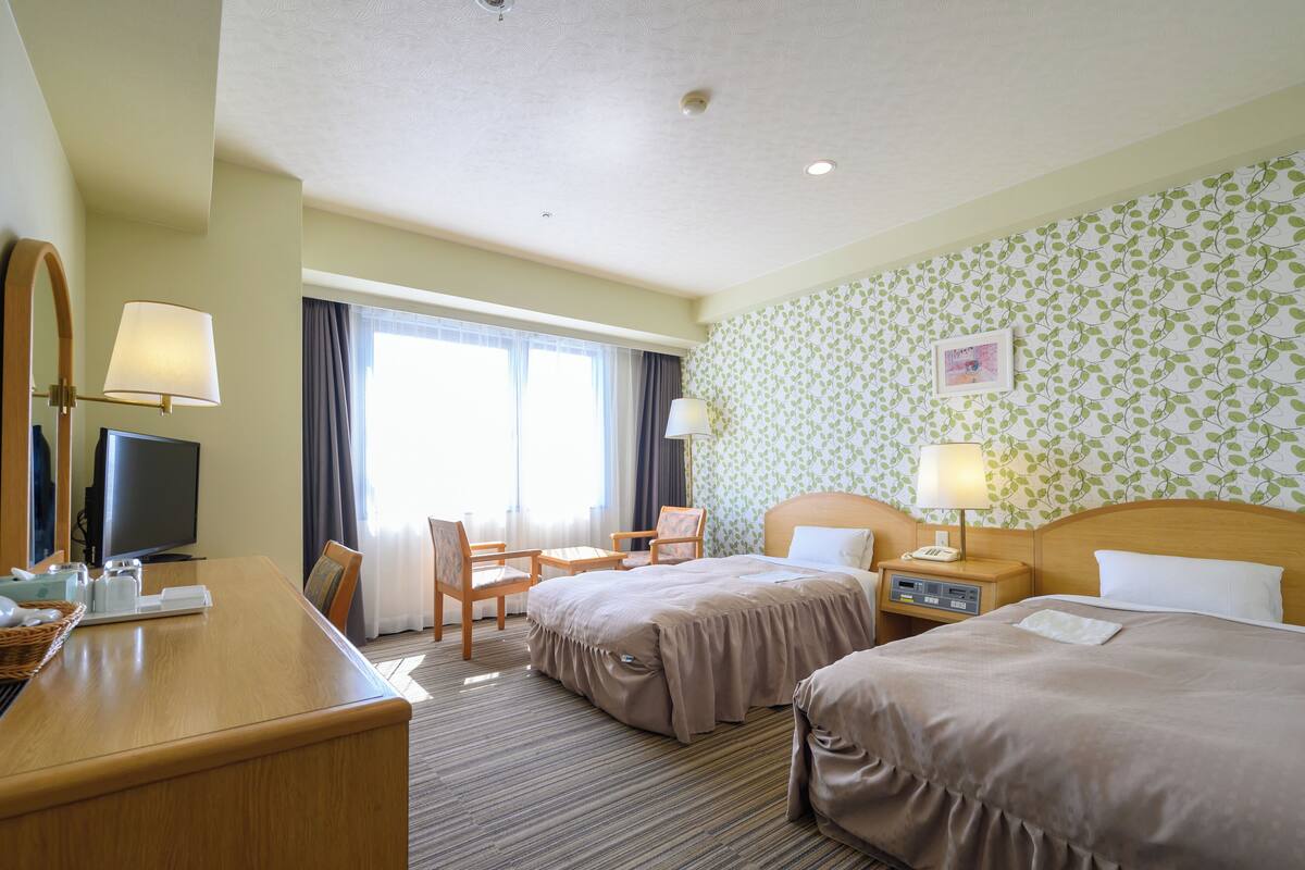 Een hotelkamer met twee bedden, een bureau, een televisie en een raam met gordijnen.