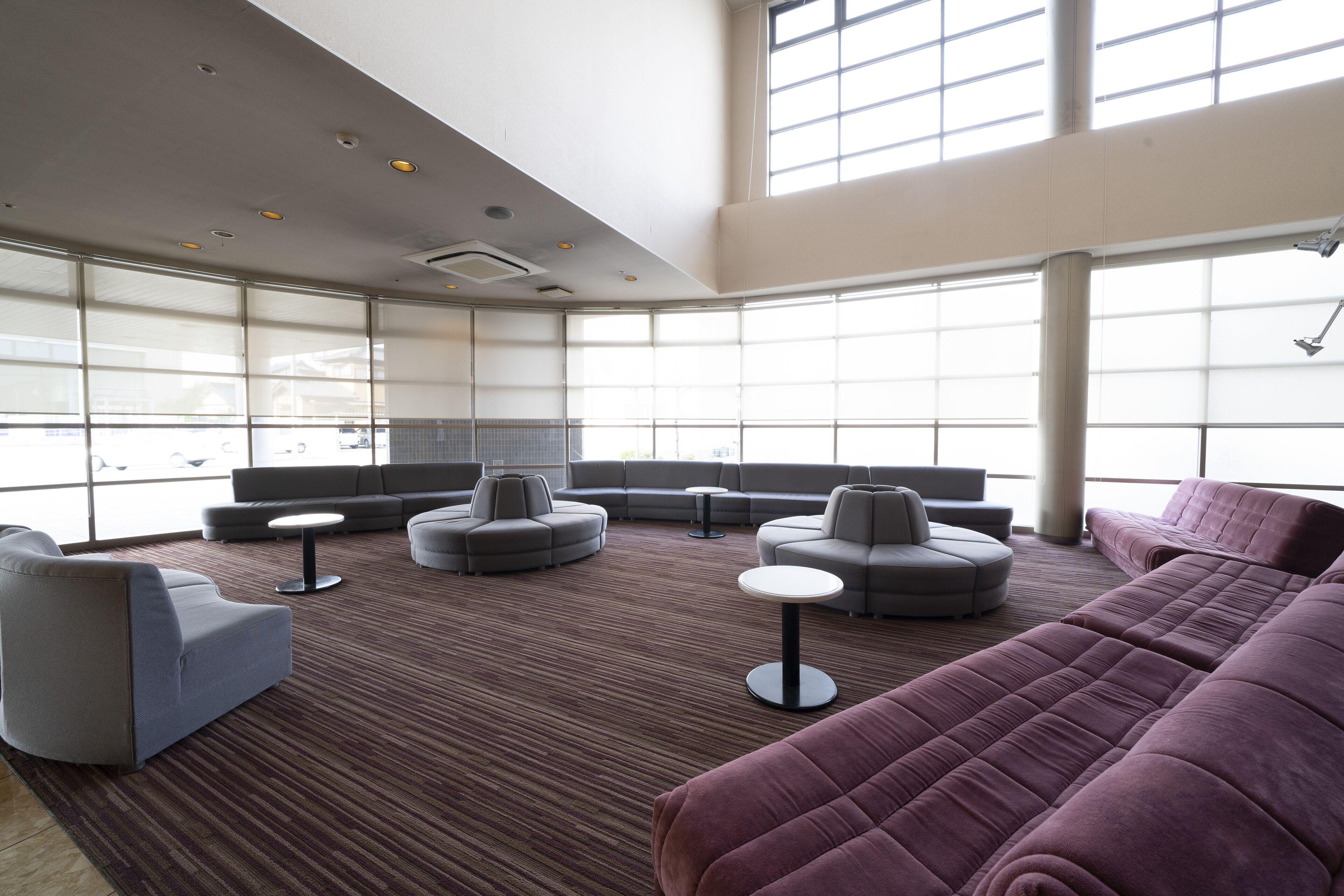 Un espace de détente moderne, doté de canapés et de fauteuils, de grandes fenêtres et d’un sol recouvert de moquette.