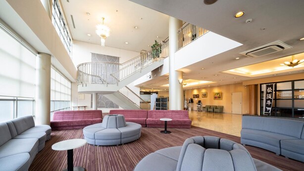 Een ruime lobby met moderne zitplaatsen, een centrale trap en een bord met daarop de naam van een restaurant.
