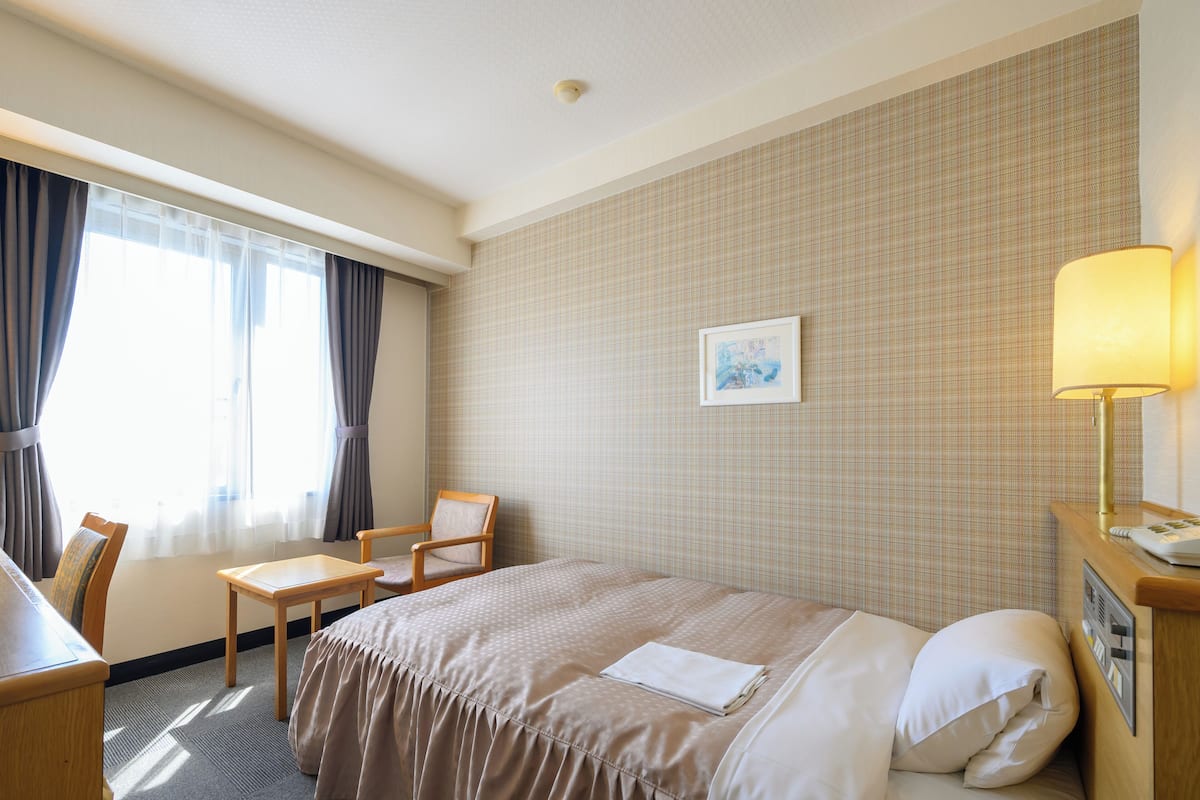 Een hotelkamer met een bed, een bureau, een stoel, een lamp en een schilderij aan de muur.